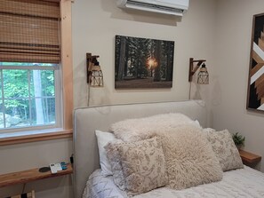 Ein Schlafzimmer mit einem Bett, einem Fenster mit Jalousien, einer Wandklimaanlage und zwei Wandleuchten.
