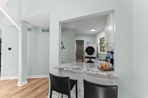 Eine moderne Küche mit Marmorarbeitsplatte, zwei schwarzen Barhocker, einer integrierten Waschmaschine und einem Fenster mit Blick.