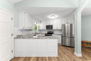 Une cuisine avec des meubles blancs, un réfrigérateur en acier inoxydable et un plan de travail en granit.