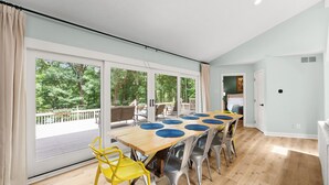 Un espace repas comprenant une grande table, des chaises et donnant sur une terrasse et des arbres.