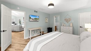 Une chambre avec un grand lit, une commode, une console et un téléviseur fixé au mur.