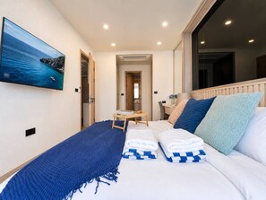 A hotel room with a bed, a TV mounted on the wall, a small table with a tray, and a window with a view of the sea. - 1BR Felix Suite Bangtao Beach (Tambon Choeng Thale)