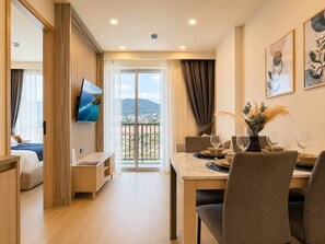 A hotel room with a balcony, a dining area with a table set for two, and a bed with a view. - 1BR Felix Suite Bangtao Beach (Tambon Choeng Thale)