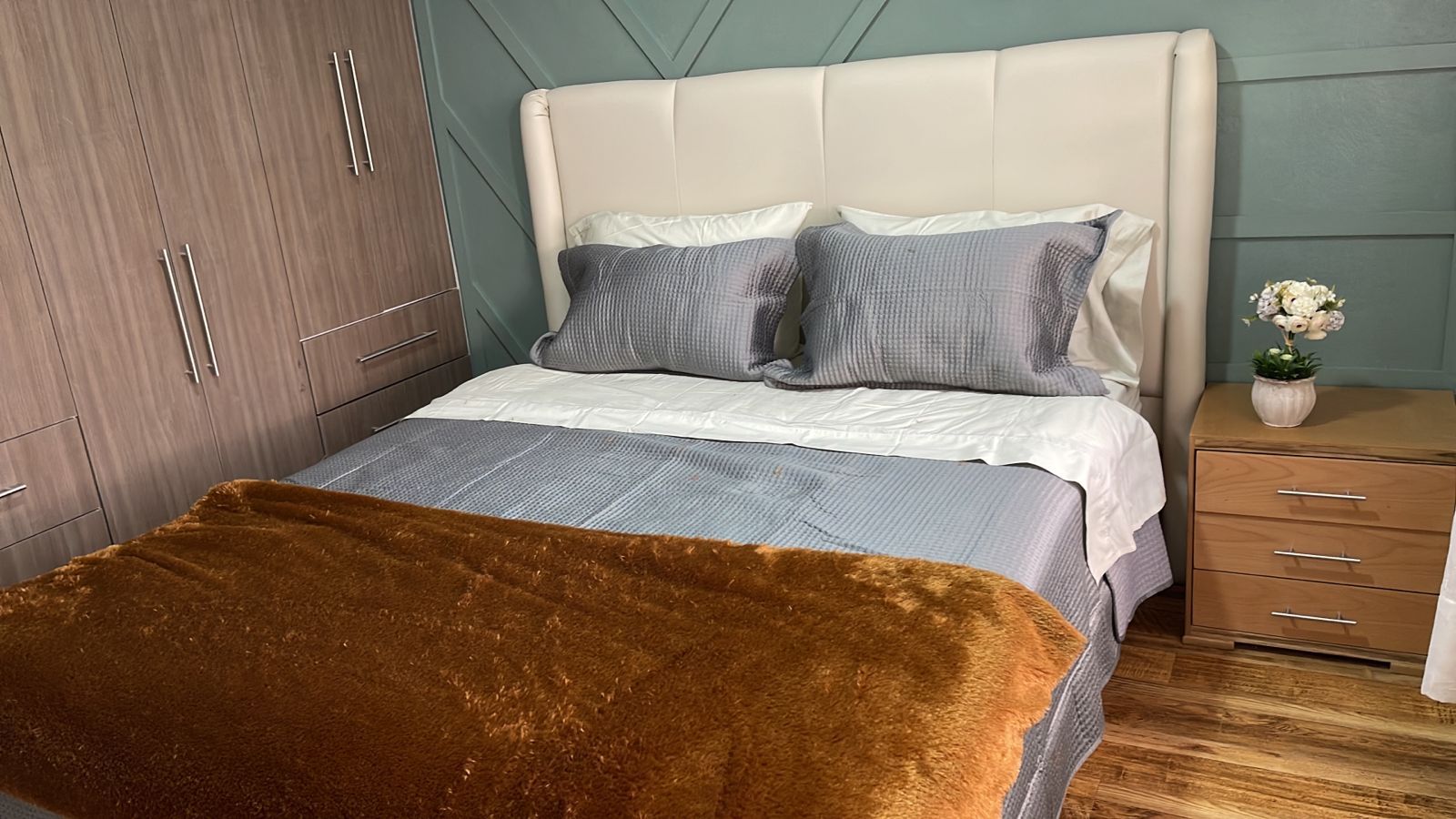 A bedroom with a bed, a nightstand, a dresser, and a potted plant.