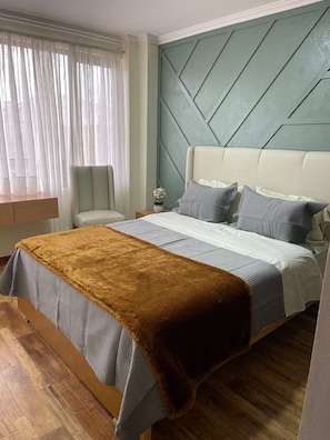 Een slaapkamer met een bed, nachtkastje, stoel en raam met gordijnen.