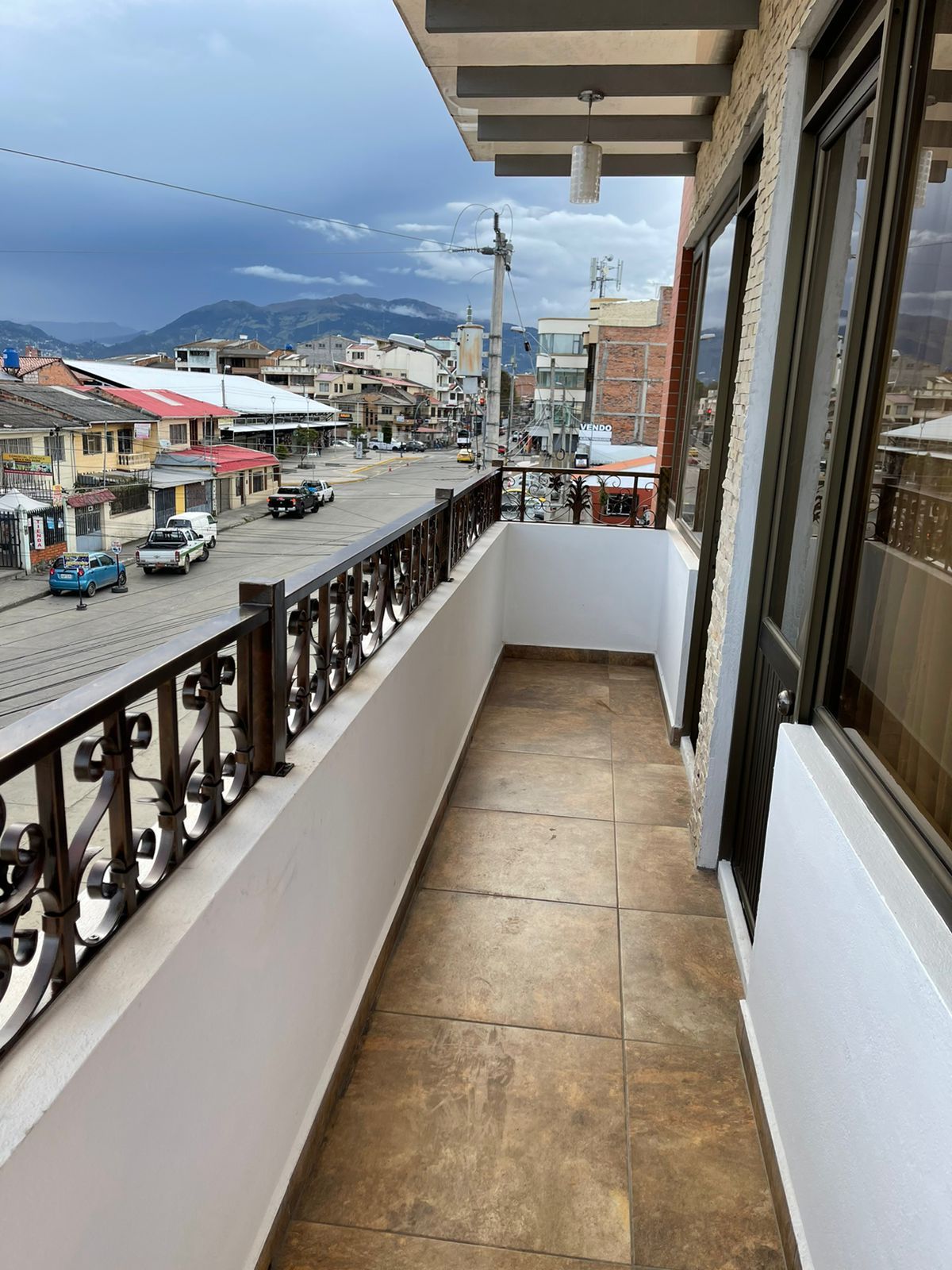A balcony with a metal railing, a view of a street with cars and buildings, and a mountain in the distance.