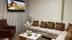 Een moderne zithoek met een bank, fauteuil, salontafel en een flatscreen televisie aan de wand.