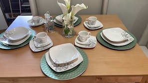 Een eettafel gedekt met witte borden, kommen en bekers, met een vaas met witte bloemen en zout- en peperstrooiers.