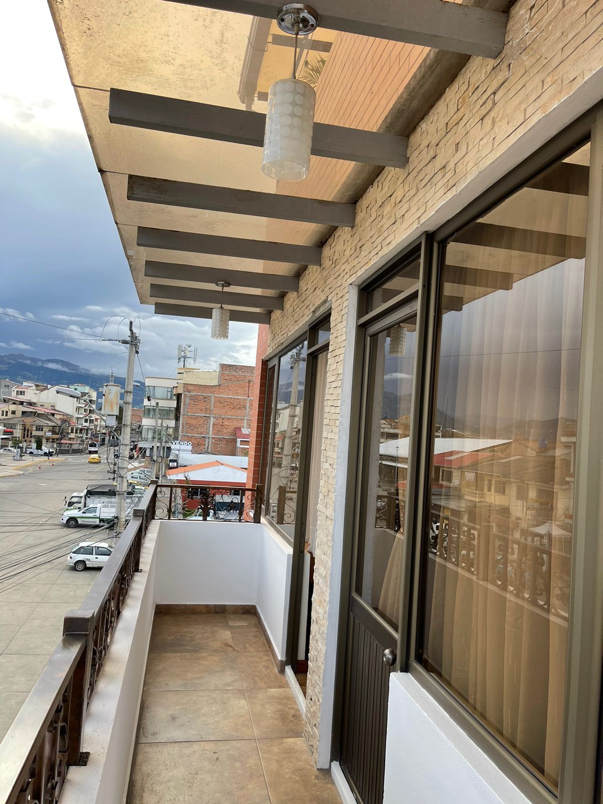 En balkon med udsigt over en travl gade, store vinduer og et hængende lysarmatur.