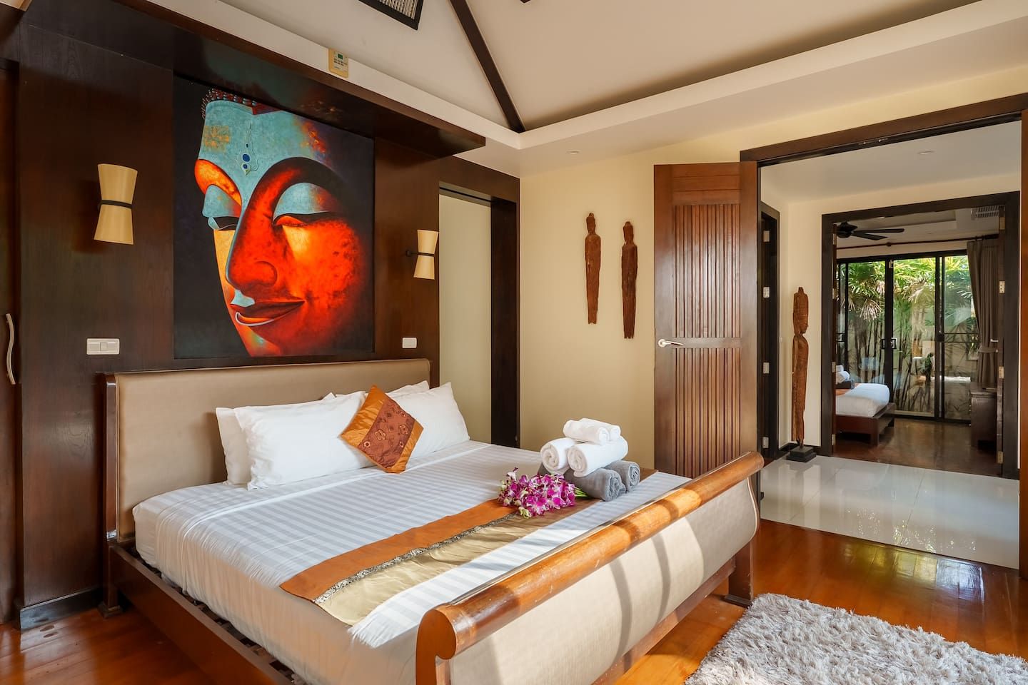 Une chambre spacieuse avec un grand lit, un tableau au-dessus de la tête de lit et une vue sur le jardin par une porte ouverte.