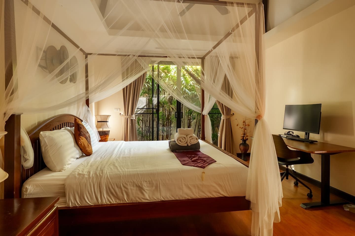A bedroom with a bed, bedside table, TV, and a view of greenery outside.