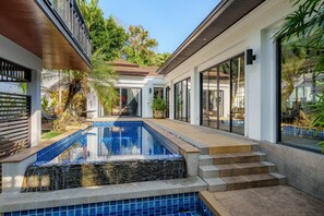 Ein moderner Poolbereich mit freiem Blick auf den Pool, Treppen zu einer überdachten Terrasse und umliegender Bepflanzung.