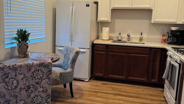 Una cucina con mobili bianchi, un frigorifero, un fornello e un'area pranzo con tavolo e sedia.