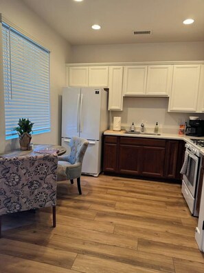 A kitchen with white cabinets, a refrigerator, a stove, and a dining area with a table and chair.
