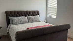 Una camera da letto con un letto, una finestra con persiane, una bocchetta di ventilazione a soffitto e un pavimento rivestito di moquette.