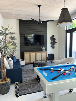 Ein modernes Wohnzimmer mit Billardtisch, Deckenventilator und Fernseher.