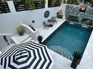 Uma área moderna com piscina ao ar livre, design de azulejos geométricos, assentos e lareira.