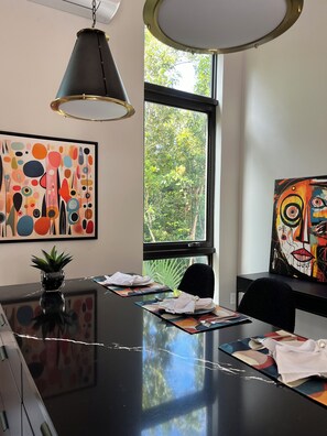 Ein moderner Konferenzraum mit einem schwarzen Tisch, zwei Gemälden, einem Topf mit einer Pflanze und einem Fenster mit Blick auf Bäume.
