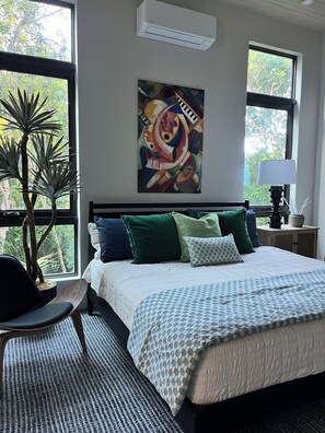 Een slaapkamer met een bed, een stoel, een kamerplant, een schilderij en een raam.