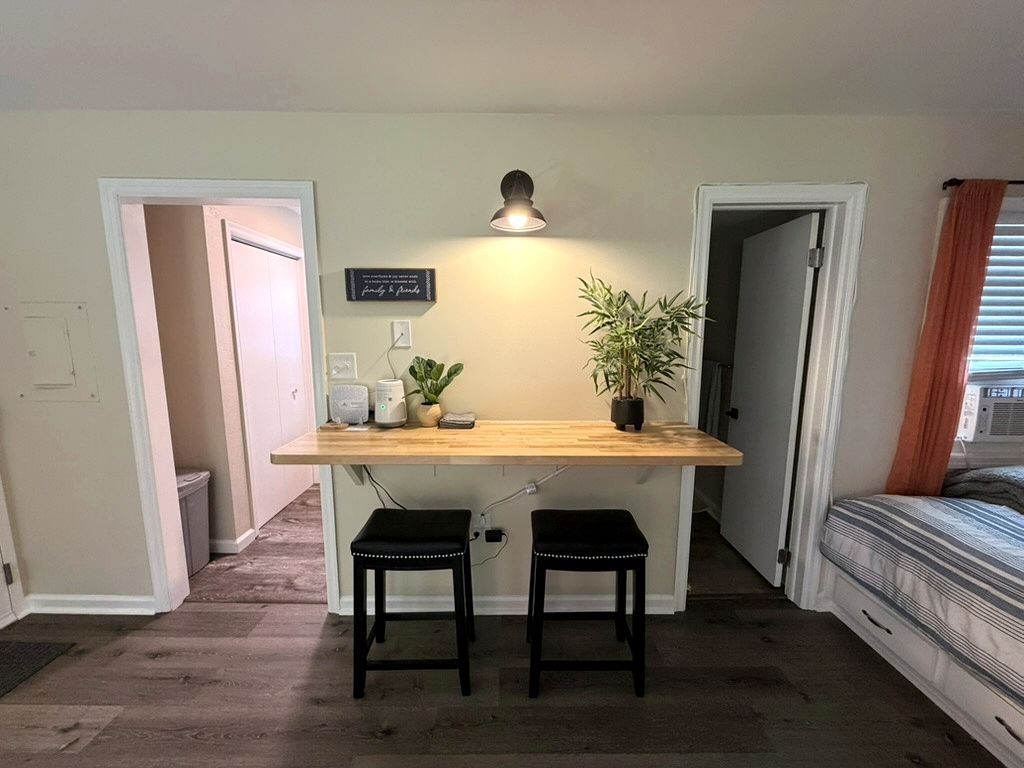 A compact room with a kitchenette, a single bed, and a small seating area with stools.