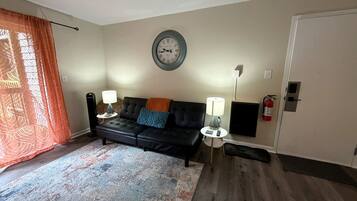 A living room with a black sofa, patterned rug, wall clock, and a door.