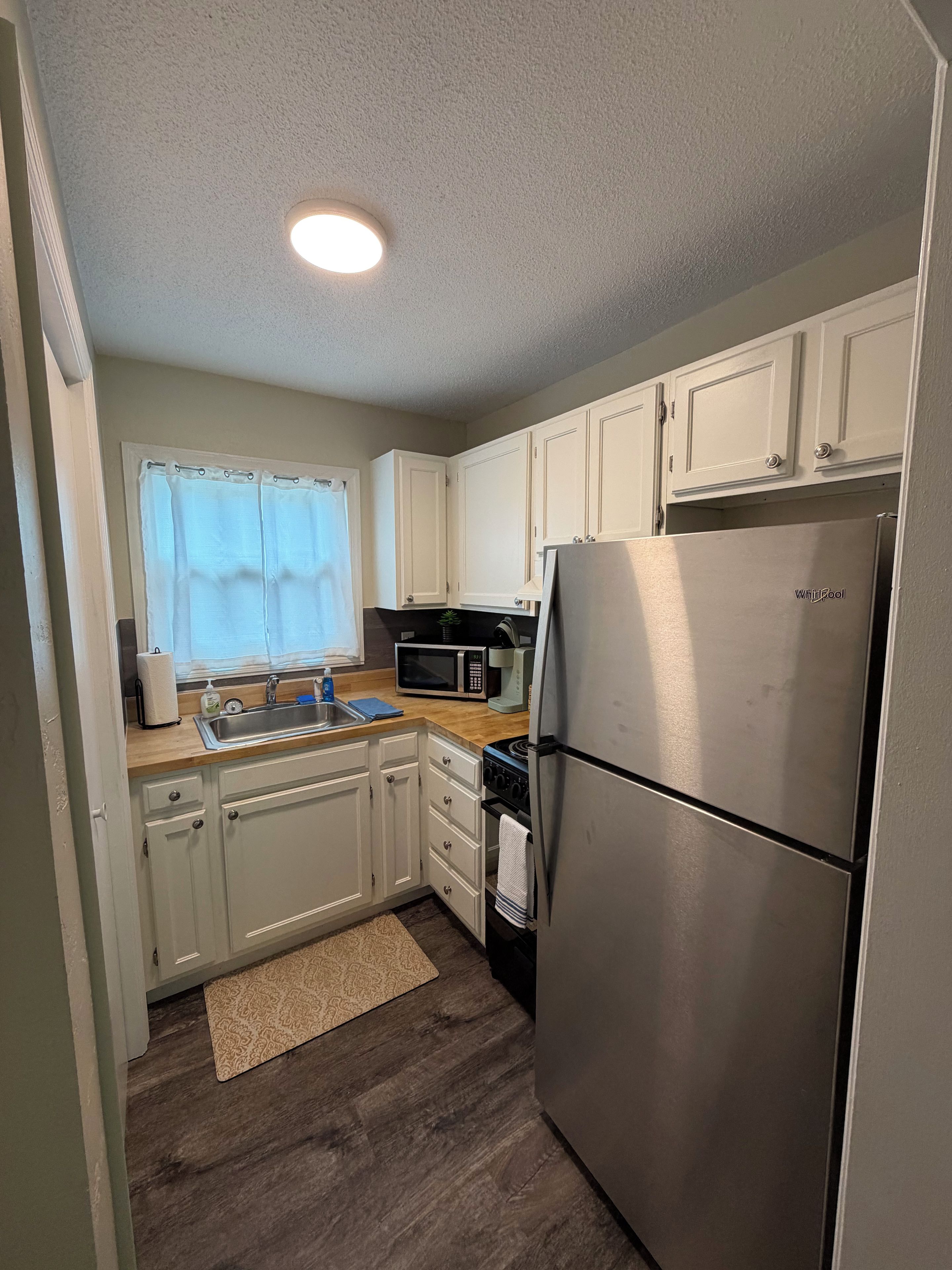 A compact kitchen with white cabinets, a stainless steel refrigerator, a microwave, and a sink.