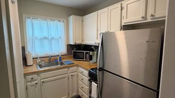 A compact kitchen with white cabinets, a stainless steel refrigerator, a microwave, and a sink.