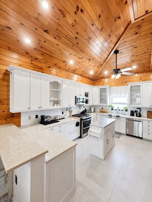 A modern kitchen with white cabinetry, a central island, and a ceiling fan. - Amazing Oceanfront Condo w Onsite Diving and Restaurant (West Bay)