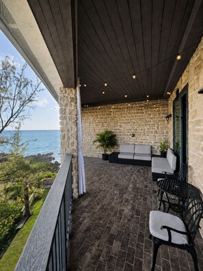 A covered outdoor seating area with stone walls, a view of the sea, and a wooden ceiling. - Amazing Oceanfront Condo w Onsite Diving and Restaurant (West Bay)