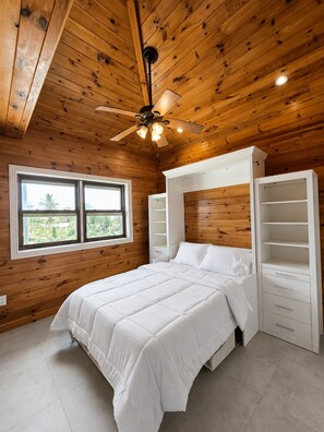 A bedroom with a bed, a ceiling fan, a window, and built-in shelving. - Amazing Oceanfront Condo w Onsite Diving and Restaurant (West Bay)