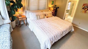 Un dormitorio con una cama grande, mesitas de noche, una lámpara y una planta en maceta.