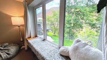 A room with a large window, a bench, a lamp, and a plush toy.