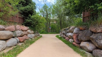 A paved pathway flanked by stone walls and dense foliage, leading into a wooded area.