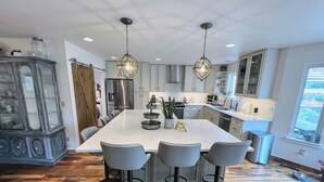 Una cocina moderna con una isla central, taburetes de bar, un refrigerador e iluminación colgante.