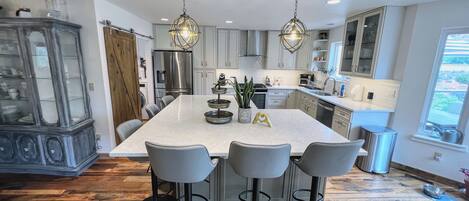 A modern kitchen with a central island, bar stools, a refrigerator, and pendant lighting.