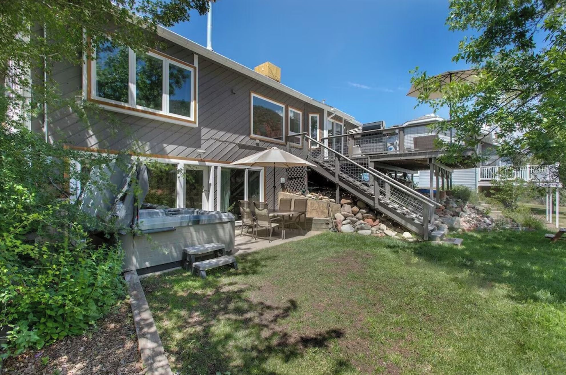 Ein zweistöckiges Haus mit Terrasse, Sitzgelegenheiten im Freien und einer Treppe zu einer Außengaststätte.