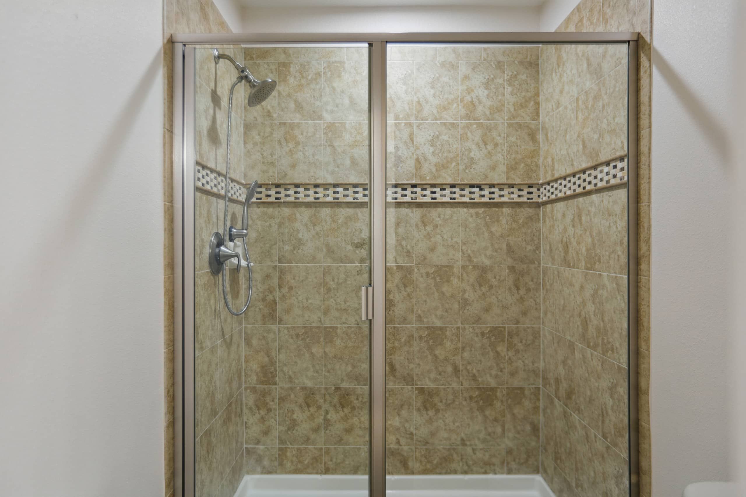 A glass-enclosed shower with a handheld showerhead and a wall-mounted faucet.