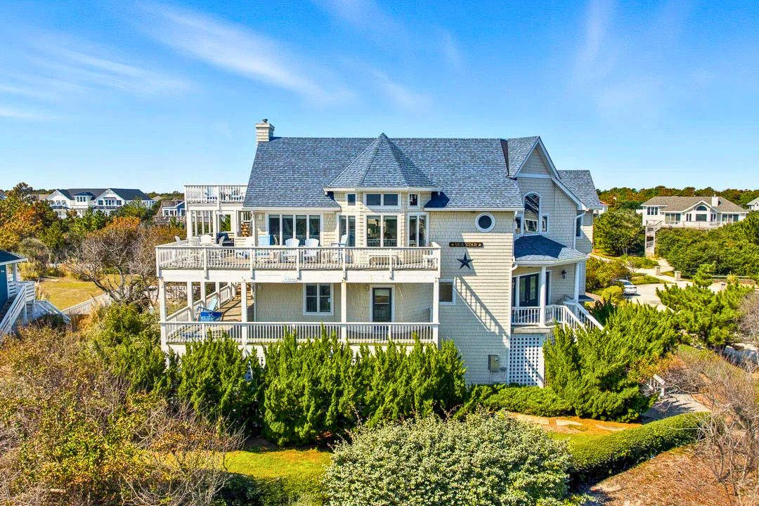A large, multi-story house with a balcony, surrounded by greenery.
