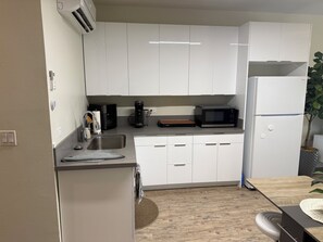 Cuina moderna amb armaris blancs, un rentapeus d'acer inoxidable, un microones i un frigorífic.