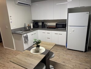 Eine moderne Küche mit weißen Schränken, einer Mikrowelle, einer Kaffeemaschine und einem Kühlschrank.