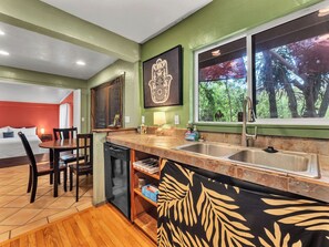 A kitchen with a dining area, a dishwasher, and a window with a view of trees. - Authentic 5-bedroom estate in Kailua-Kona Living in Harmony with nature (Kailua-Kona)