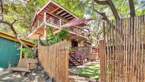 A two-story wooden house with a balcony, surrounded by a bamboo fence, and a small garden area with a bench and stepping stones. - Authentic 5-bedroom estate in Kailua-Kona Living in Harmony with nature (Kailua-Kona)