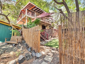 A two-story wooden house with a balcony, surrounded by a bamboo fence, and a small garden area with a bench and stepping stones. - Authentic 5-bedroom estate in Kailua-Kona Living in Harmony with nature (Kailua-Kona)