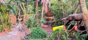 A rustic outdoor area with a yellow vehicle, a wooden structure, and dense greenery. - Authentic Eco-estate in Kona sleeps 14 -Living in Harmony with nature by the sea (Kailua-Kona)