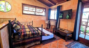 A room with a bed, a chair, a small table, and a TV. - Authentic Eco-estate in Kona sleeps 14 -Living in Harmony with nature by the sea (Kailua-Kona)