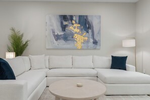A modern living room with a sectional sofa, a round coffee table, a floor lamp, and a large abstract painting. - Luxury 5BR Resort with Hot Tub 12 miles from ATT Stadium Sleeps 10 (Mansfield)