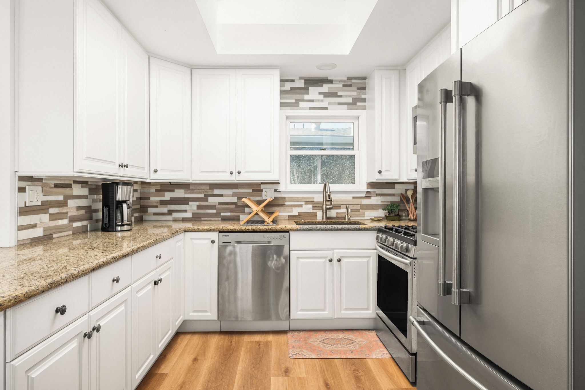 A modern kitchen with white cabinets, stainless steel appliances, a dishwasher, and a coffee maker.