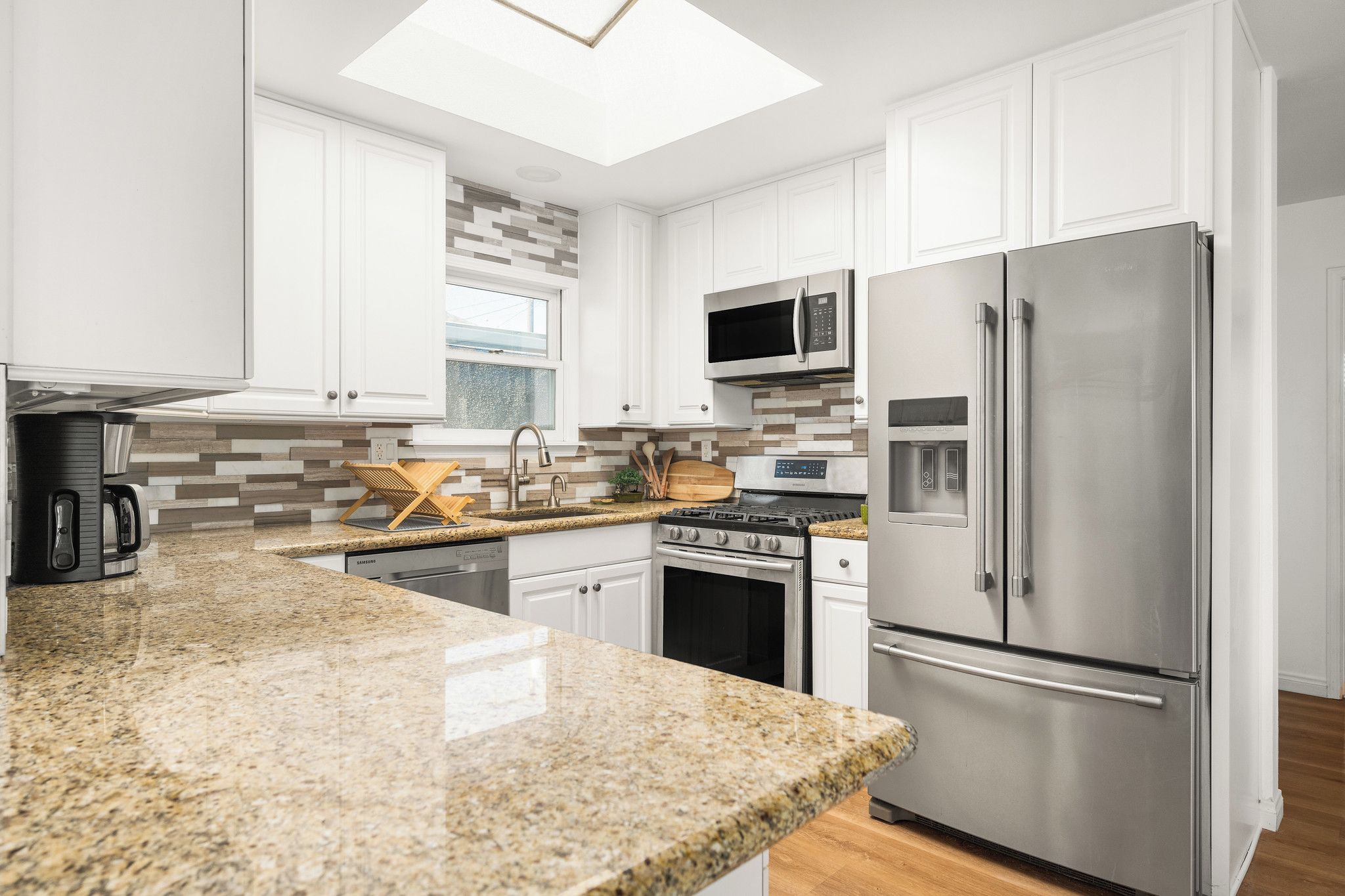 A modern kitchen with white cabinets, stainless steel appliances, and a granite countertop.