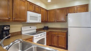 A kitchen with wooden cabinets, a white microwave, a stove, a sink, and a refrigerator. - 2-Bedroom South Tahoe Resort Next to Beach & Zephyr Cove - AC & fitness room (Zephyr Cove)