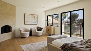 Ein modernes Schlafzimmer mit Kamin, zwei Sesseln, einem Bett und einem großen Fenster mit Blick.